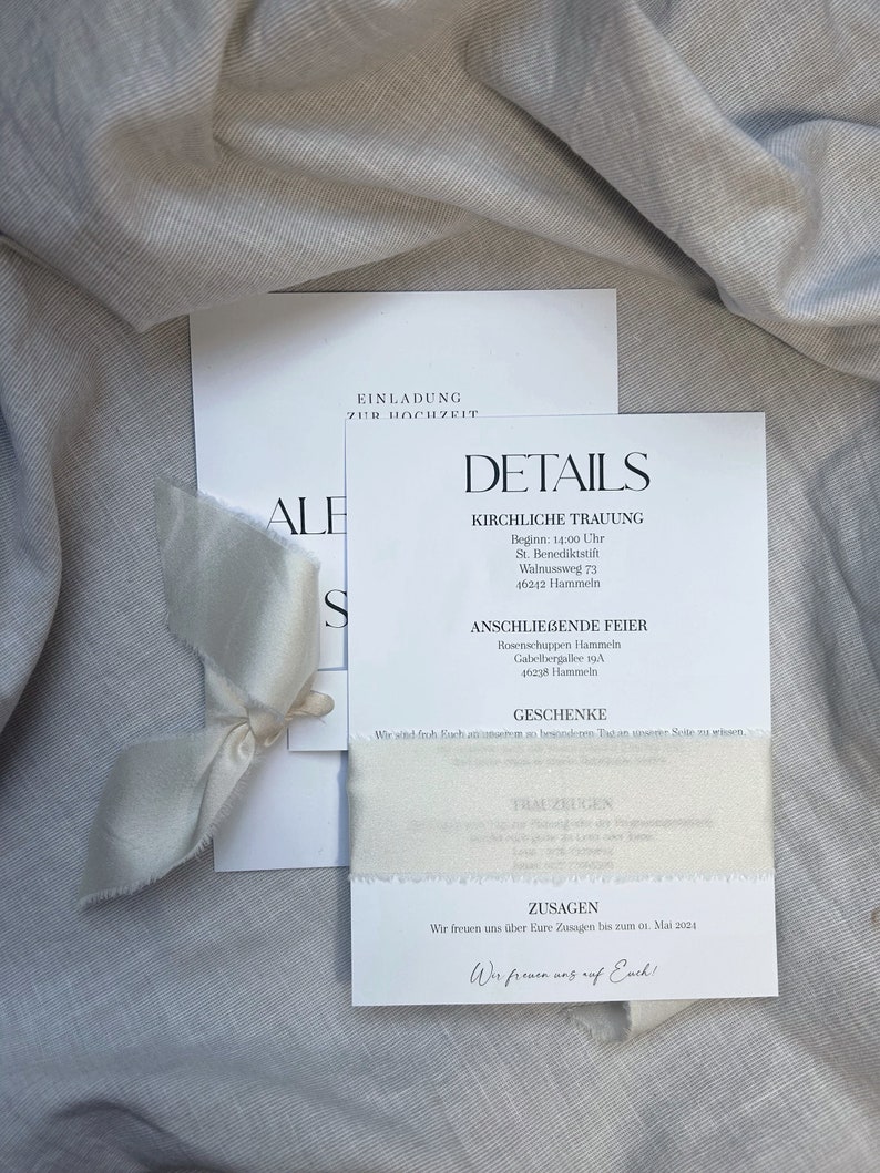 May include: A white wedding invitation with the text "Einladung zur Hochzeit" (Invitation to the wedding) and details about the ceremony and reception. The invitation is decorated with a white ribbon.