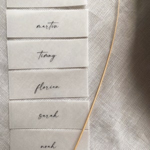 Puede incluir: Seis tarjetas de lugar blancas con nombres en caligraf&iacute;a negra: Thomas, Martin, Timmy, Florian, Sarah y Noah.