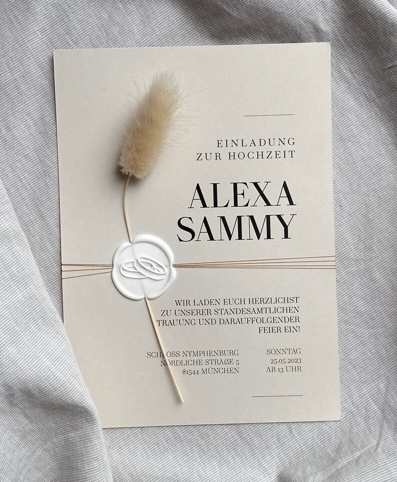 May include: A beige wedding invitation with a wax seal and a dried flower. The invitation reads "Einladung zur Hochzeit Alexa Sammy" and includes the date and time of the wedding: "Sonntag 25.05.2023 AB 13 UHR". The wedding will take place at Schloss Nymphenburg, Nordliche Strasse 5, 81544 M&uuml;nchen.