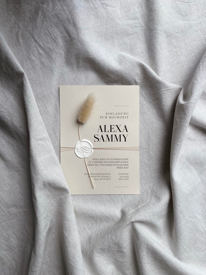 May include: A white wedding invitation with a simple design. The invitation features the text "Einladung zur Hochzeit" and the names "Alexa Sammy". The invitation also includes the date and time of the wedding.