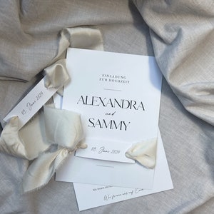 May include: A white wedding invitation with black text. The invitation reads "Einladung zur Hochzeit" which translates to "Invitation to the Wedding". The names Alexandra and Sammy are printed in large, bold letters. The date "08. June 2024" is printed on the invitation and on a separate tag.