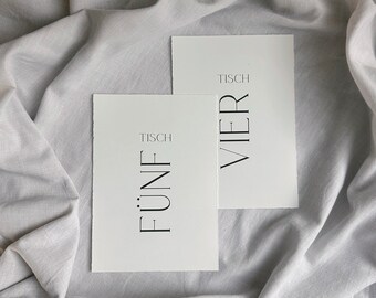 Könnte beinhalten: Zwei weiße Karten mit schwarzem Text. Die obere Karte sagt "Tisch Vier" und die untere Karte sagt "Tisch Fünf".