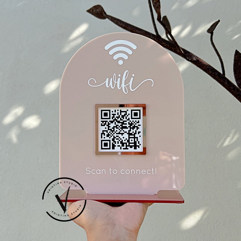 May include: A pink acrylic sign with a rounded top and a white wifi symbol. The sign says "wifi" in white cursive lettering. A square, silver frame with a black and white QR code is in the centre of the sign. The text "Scan to connect!" is below the QR code.