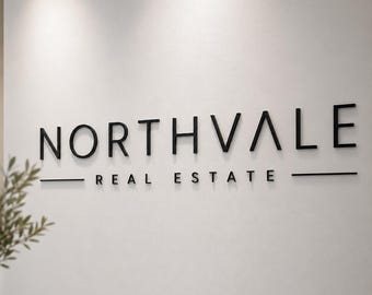 Può includere: Un'insegna a parete con lettere nere tridimensionali che formano la parola NORTHVALE in un carattere sans-serif, posizionata sopra il testo più piccolo REAL ESTATE, fiancheggiato da due linee orizzontali su una parete chiara.