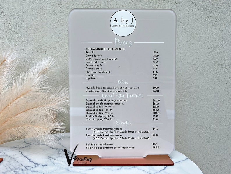 May include: A white acrylic sign with black text listing prices for anti-wrinkle treatments, dermal filler treatments, and specials. The sign is on a wooden stand.