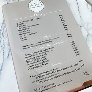 May include: A price list for anti-wrinkle treatments, dermal filler treatments, and specials at a business called "A by J Aesthetics by Janice". The list includes prices for treatments such as brow lift, crow's feet, DOA (downturned mouth), forehead lines, gummy smile, hay fever treatment, lip flip, and lip lines. Dermal filler treatments include dermal cheeks and lip augmentation, dermal cheeks augmentation, dermal lip filler 0.5ml, dermal lip filler 1ml, dermal lip filler 2ml, jawline sculpting, and chin sculpting. Specials include 3 anti-wrinkle treatment areas and 2 anti-wrinkle treatment areas with the option to add dermal lip filler 0.5ml or 1ml. The list also includes prices for a full facial consultation and follow-up appointments.