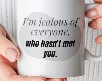 May include: A white ceramic mug featuring a light gray organic-shaped background graphic with the black printed text: I'm jealous of everyone, who hasn't met you. The mug has a standard handle on the right side and a smooth, glossy finish.