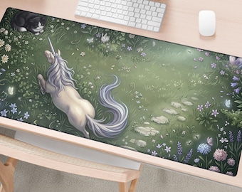 May include: A rectangular desk mat featuring a detailed illustration of a white unicorn with a flowing mane in a lush green meadow. The scene includes a black and white cat, a small rabbit, butterflies, various wildflowers, and a stone path.