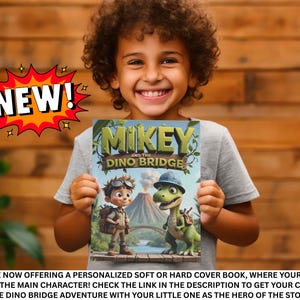 A young boy is holding a book titled "Mikey and the Dinosaur Bridge" and smiling, with a large "NEW!" explosion graphic above him.