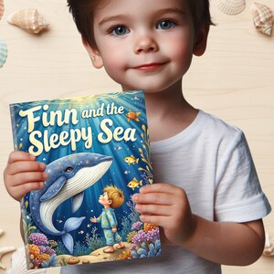 May include: A children's book titled "Finn and the Sleepy Sea" featuring a blue whale and a young boy in pajamas. The cover art is vibrant with underwater imagery, including coral and fish. The book is held by a child.