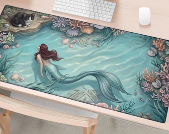 May include: A rectangular desk mat featuring an underwater scene with a mermaid with long brown hair and a teal tail swimming in clear blue water. The scene includes a black and white cat on a rock, colorful coral reefs, seashells, and a sea turtle.