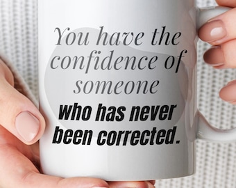 May include: A white ceramic mug featuring the black printed text: You have the confidence of someone who has never been corrected. The mug has a standard cylindrical shape with a side handle and a smooth, glossy finish throughout the exterior surface.