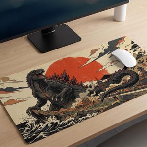 May include: A rectangular desk mat featuring a graphic illustration of a large, dark, reptilian monster standing on a rocky shore with crashing waves. A large red sun sits in the background behind the creature, with stylized clouds and a traditional building structure visible on the right side.