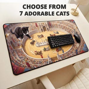 May include: A rectangular desk mat featuring a large black and white kitten overlooking a Roman colosseum scene with chariot races and spectators. The text CHOOSE FROM 7 ADORABLE CATS is printed above the mat on the desk surface.