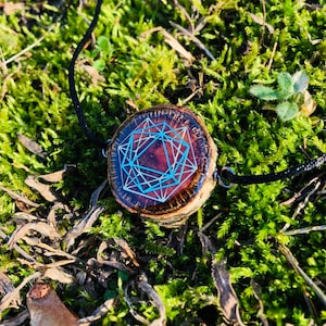 May include: A wooden pendant necklace with a geometric design. The pendant is a cross-section of a tree branch, with a dark brown resin center and a light blue geometric pattern. The necklace cord is black.