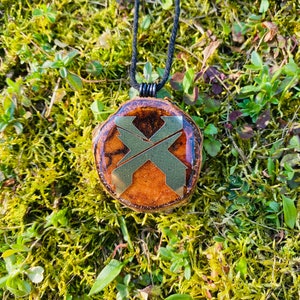 May include: A wooden pendant necklace with a gold-colored X design. The pendant is round and has a brown and orange wood grain pattern. The necklace is made with black cord.