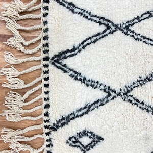 May include: White and black Moroccan rug with a diamond pattern and fringe on the edges.
