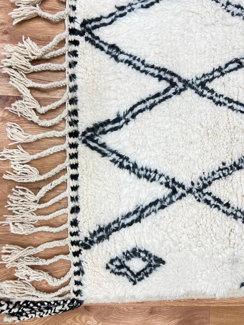 May include: White and black Moroccan rug with a diamond pattern and fringe on the edges.