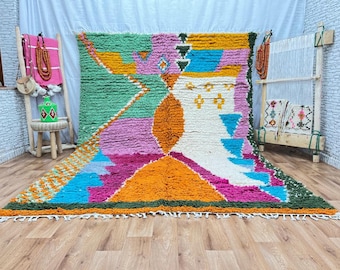 May include: A colourful Moroccan rug with geometric patterns in shades of green, pink, orange, blue, and white. The rug has a fluffy texture and is made with hand-woven wool.