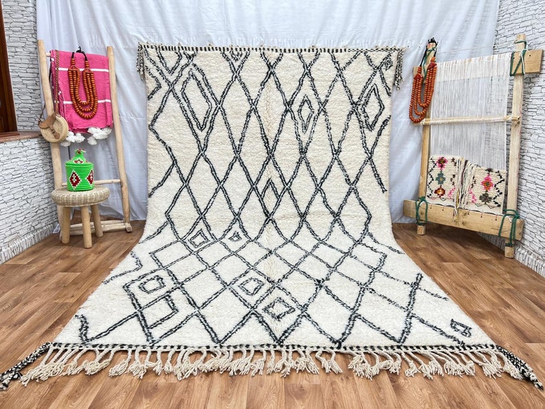 May include: A white and black Moroccan rug with a diamond pattern. The rug has a fringe border and is made of wool.