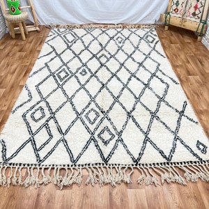 May include: A white and black Moroccan rug with a diamond pattern and fringe. The rug is made of wool and has a soft, fluffy texture.