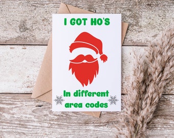 May include: A white card with green and red text that reads "I got Ho's in different area codes". A red and white Santa Claus silhouette is above the text. The card is on a wooden surface.
