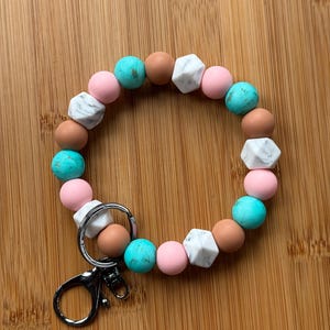 May include: A silicone beaded keychain with a silver key ring. The beads are pink, brown, turquoise, and white with a marbled pattern.