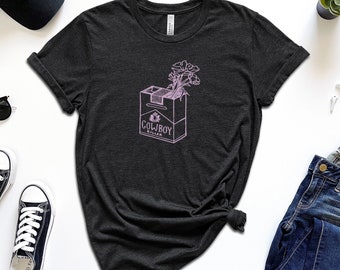 May include: A dark grey t-shirt with a pink graphic of a cigarette pack with flowers growing out of it. The text on the pack reads "Cowboy Killer".