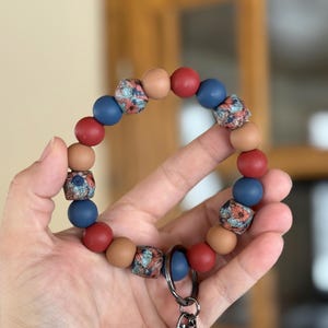 May include: A beaded keychain with a floral pattern in blue, red, and brown. The keychain has a silver metal clasp.