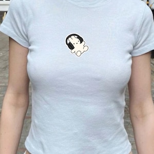 May include: Pale blue t-shirt featuring a small graphic of a white rabbit wearing black headphones. The top has short sleeves and a round neck. The material looks to be soft and lightweight.