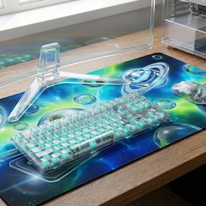 May include: A clear, transparent keyboard, mouse, and monitor stand sit on a desk. The desk has a blue and green galaxy-themed mousepad. The keyboard has light blue keys. The mouse is also transparent.