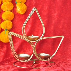 May include: A gold metal candle holder shaped like a lotus flower with three candle cups. The candle holder is on a red velvet surface.