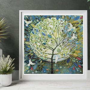 Könnte beinhalten: Ein gerahmtes Kreuzstich-Kunstwerk mit einem stilisierten Baum mit einer vollen, runden Krone. Die Blätter des Baumes sind grün und blau, vor einem hellen Hintergrund. Weiße Vögel und farbenfrohe Akzente umgeben den Baum und schaffen ein Stück zum Thema Natur.