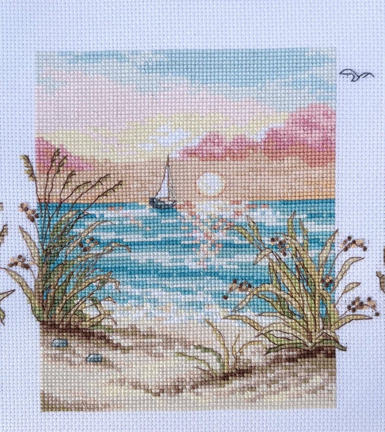 May include: Cross-stitch of a coastal scene at sunset. The image features a sailboat on the water, with the sun setting in the background. The foreground includes beach grass and sand, with a sky of pink, blue, and yellow.