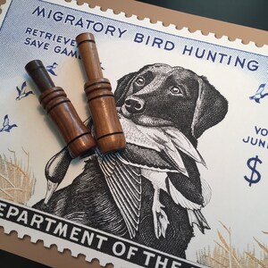 Pode incluir: Um selo de ca&ccedil;a de aves migrat&oacute;rias vintage do Departamento do Interior dos Estados Unidos que apresenta um labrador retriever preto com um pato na boca. O selo &eacute; azul e branco com o texto "Migratory Bird Hunting Stamp", "Retrieve Save Game", "Void After June 30, 196", e "$3".