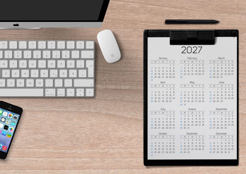 May include: A black clipboard holding a 2027 calendar with twelve months displayed in a grid. The calendar features black text on a white background, showing the year 2027 at the top, followed by monthly grids from January through December.