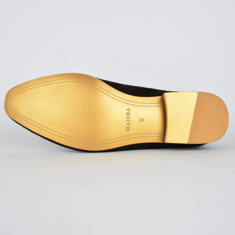 May include: The bottom of a black suede shoe with a gold sole. The sole has the brand name "MAJORA" and the size "8" printed on it.