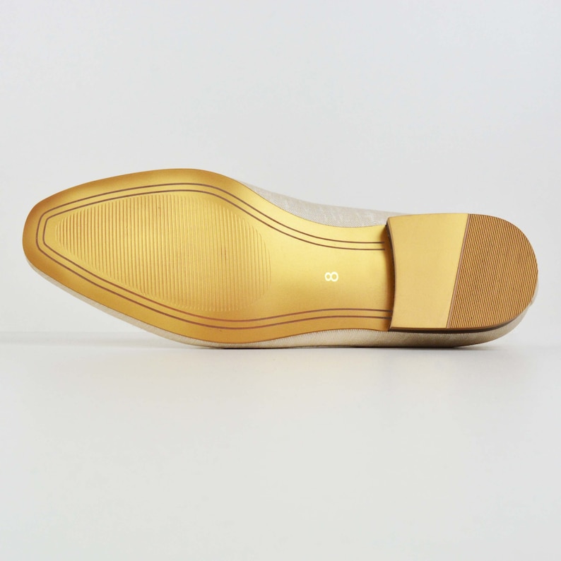 May include: The bottom of a cream-colored flat shoe with a gold sole. The sole has a textured pattern and the number "8" is printed on the sole.