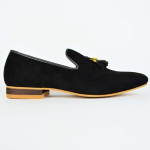 May include: Black suede loafers with a gold tassel and a brown sole.