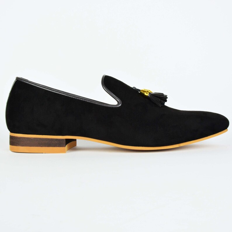 May include: Black suede loafers with a gold tassel and a brown sole.