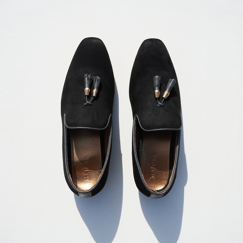 May include: A pair of black suede loafers with gold tassels. The loafers have a pointed toe and a low heel.