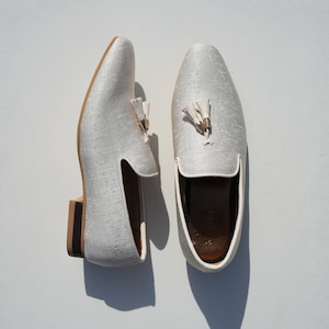 May include: A pair of white satin loafers with gold tassels. The loafers have a brown leather sole.
