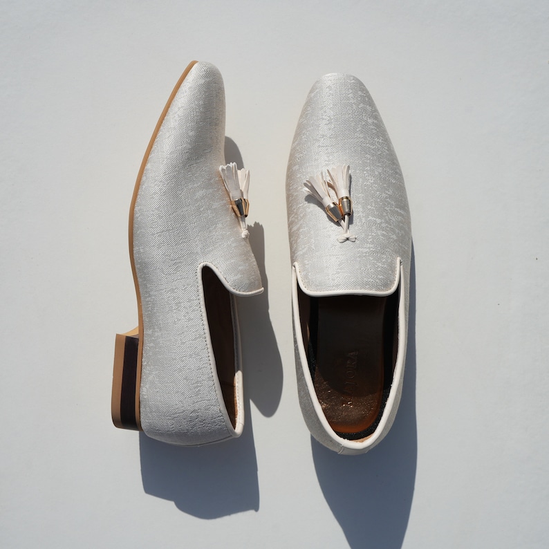 May include: A pair of white satin loafers with gold tassels. The loafers have a brown leather sole.