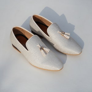 May include: A pair of white loafers with a tassel detail. The loafers have a subtle pattern and a cream-colored sole.