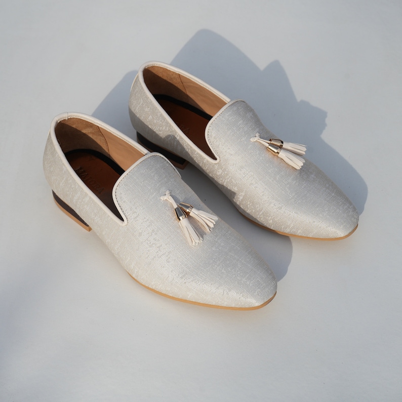 May include: A pair of white loafers with a tassel detail. The loafers have a subtle pattern and a cream-colored sole.