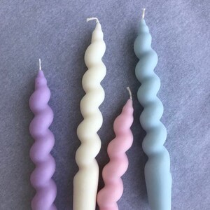 May include: Four spiral candles in different pastel colors: lavender, cream, pink, and light blue. The candles are all the same size and shape.