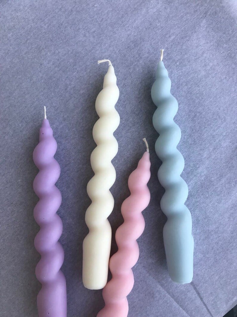 May include: Four spiral candles in different pastel colors: lavender, cream, pink, and light blue. The candles are all the same size and shape.