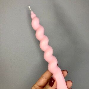May include: A pink, twisted candle with a white wick. The candle is shaped like a spiral.