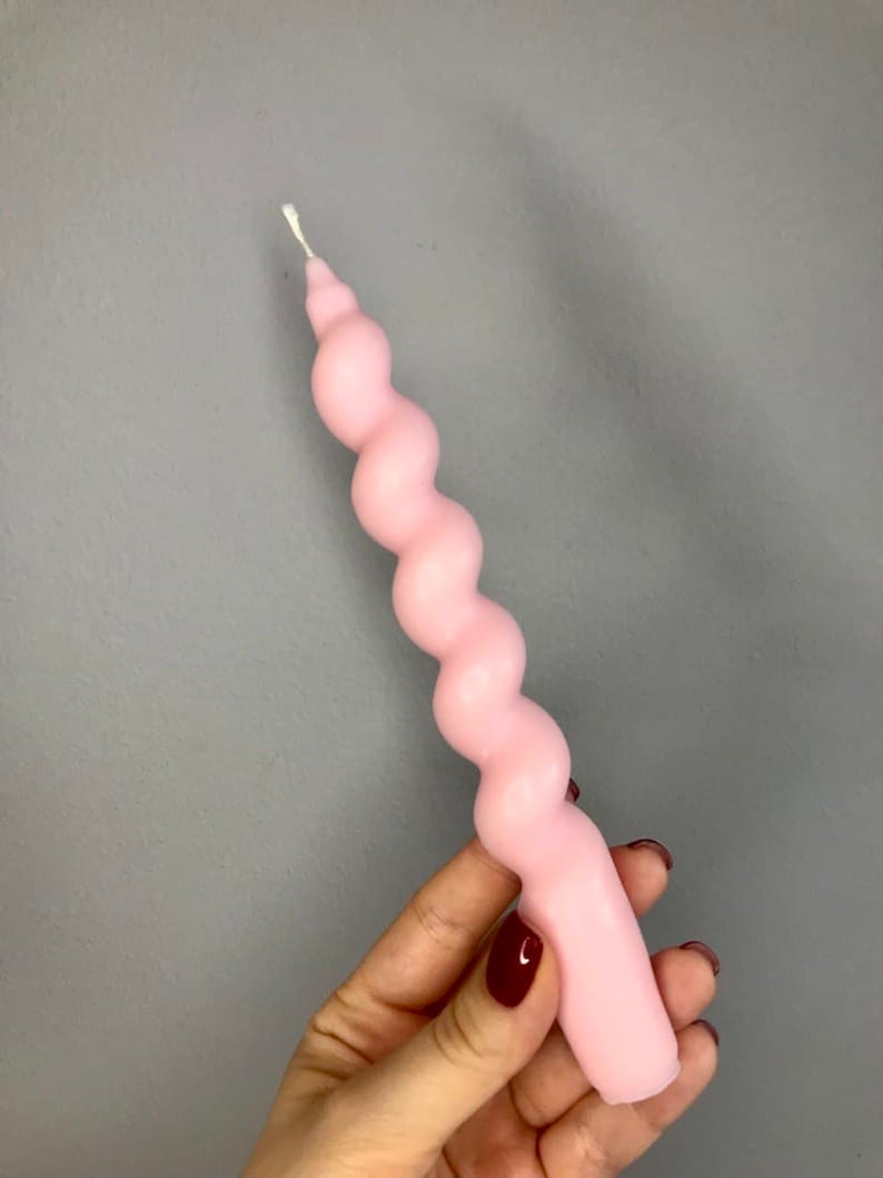 May include: A pink, twisted candle with a white wick. The candle is shaped like a spiral.