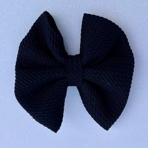 May include: A solid black bow with a textured fabric. The bow is centered and has a symmetrical design. The bow is a hair accessory.